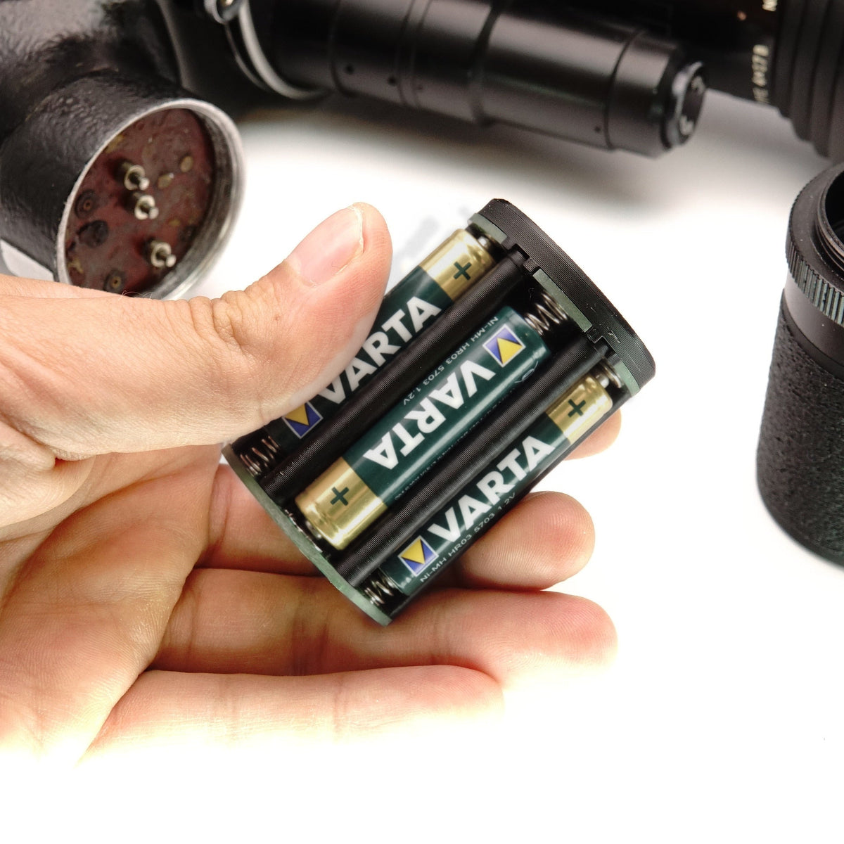 Hand hält gefüllten Batteriehalter mit eingelegten Akkus für eine Beaulieu R16 Filmkamera
