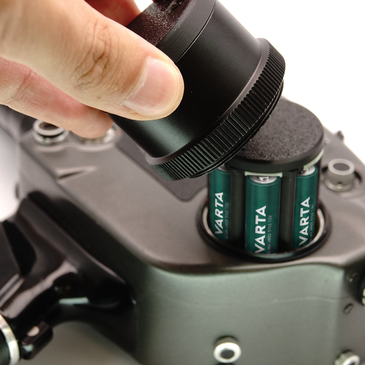 Hand setzt den zylindrischen Adapter mit eingelegten Batterien in das Batteriefach einer Beaulieu 4008 Super 8 Kamera ein