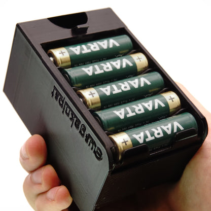 Hand hält den geöffneten Batterieadapter für Metz Mecablitz mit fünf eingelegten AA-Akkus