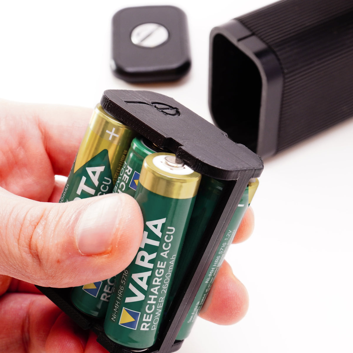 Hand hält den mit AA-Batterien bestückten Adapter für Beaulieu Super-8-Kameras vor dem Akkufach