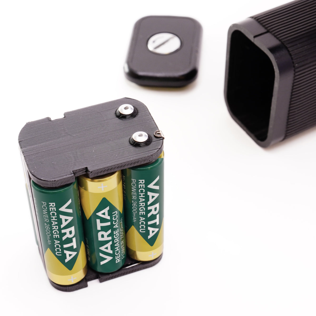 Vollbestückter Batteriehalter mit drei Varta AA Akkus neben dem geöffneten Batteriefach einer Beaulieu Kamera